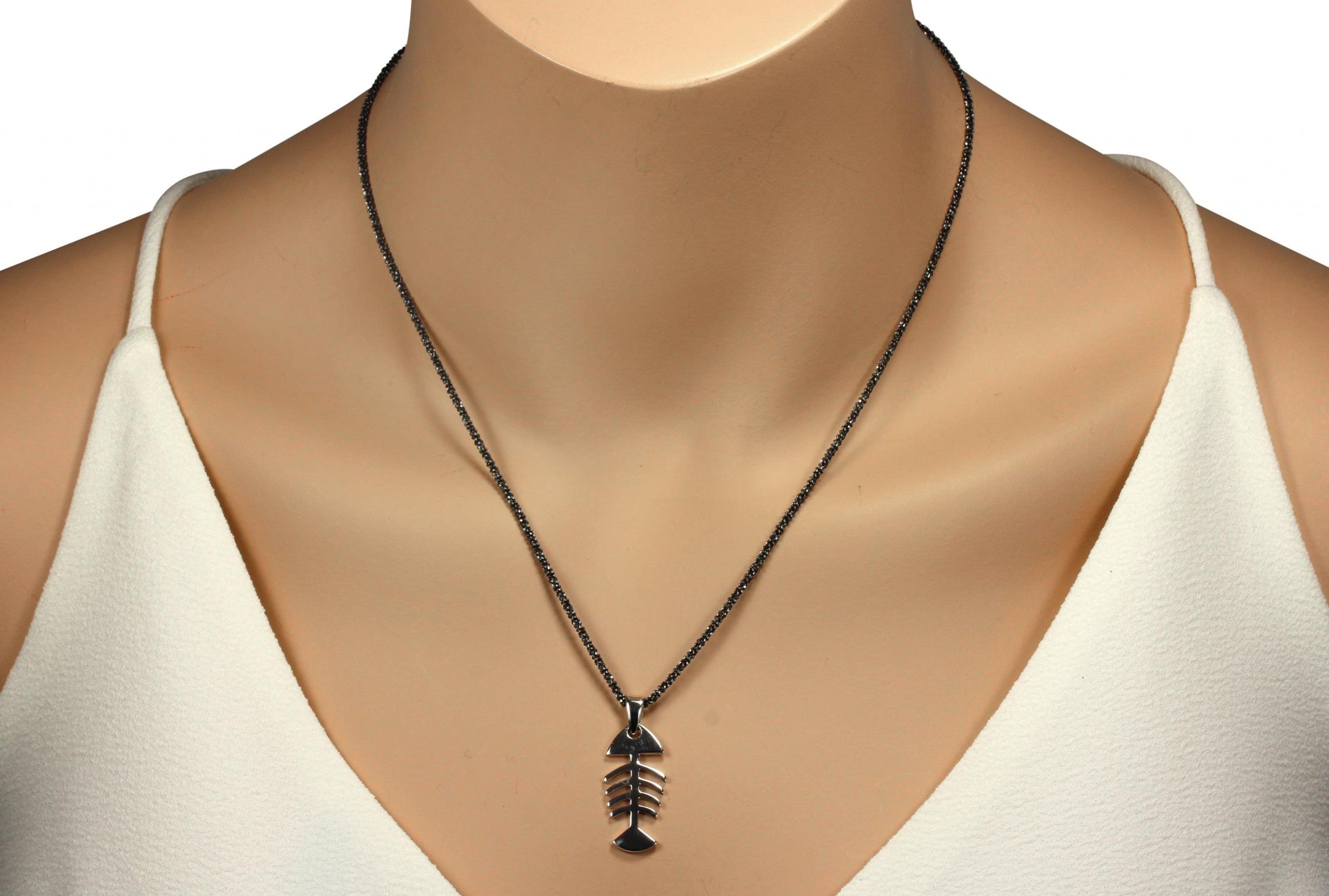 Ein Anhänger aus Silber, der einen skelettierten Fisch darstellt und eine glänzende Oberfläche aufweist, getragen mit einer geschwärzten Criss-Cross-Kette an einer Schaufesterpuppe.