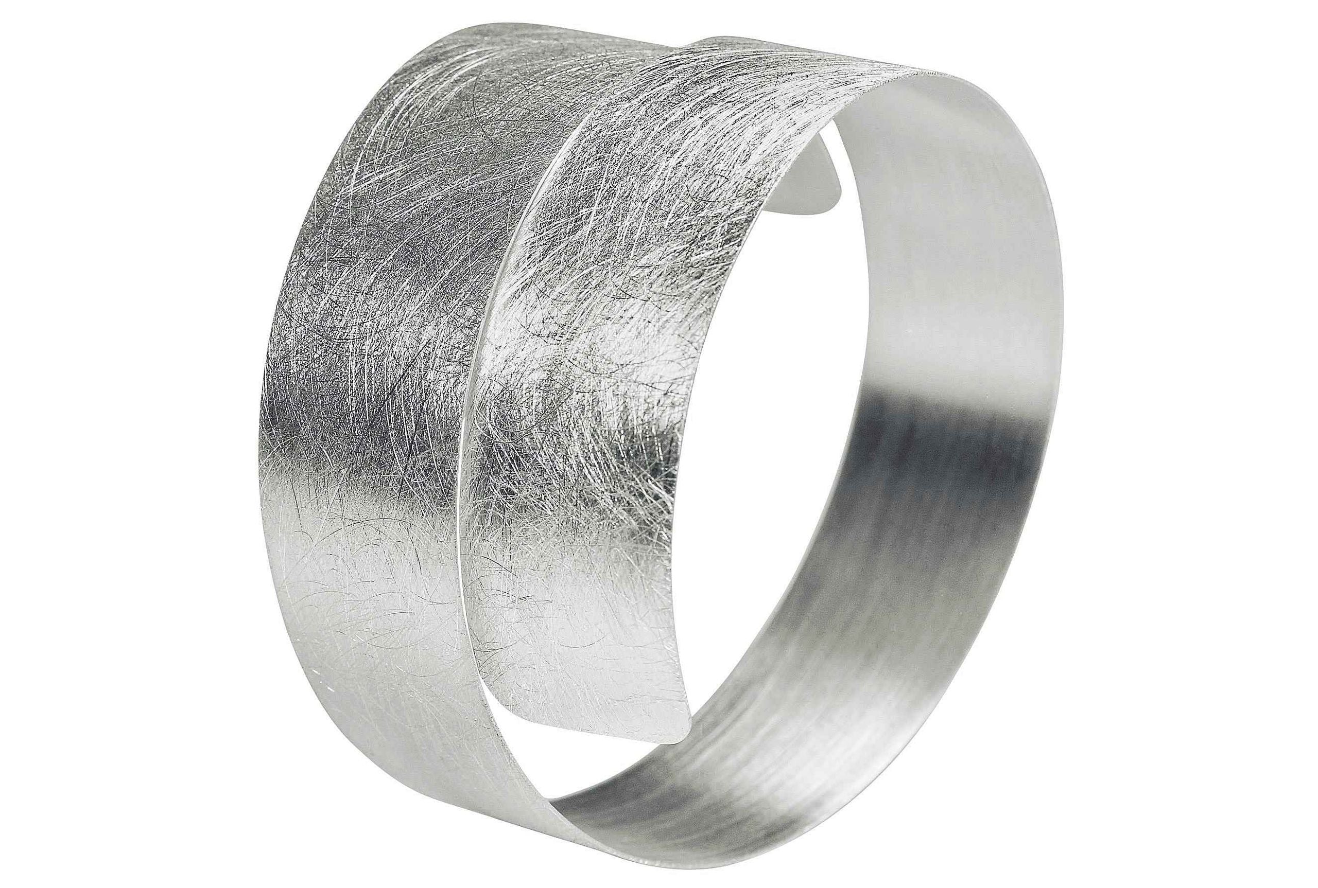 Silberner Armreif mit gebürsteter Oberfläche. Der Armreif ist schmal und spiralförmig.