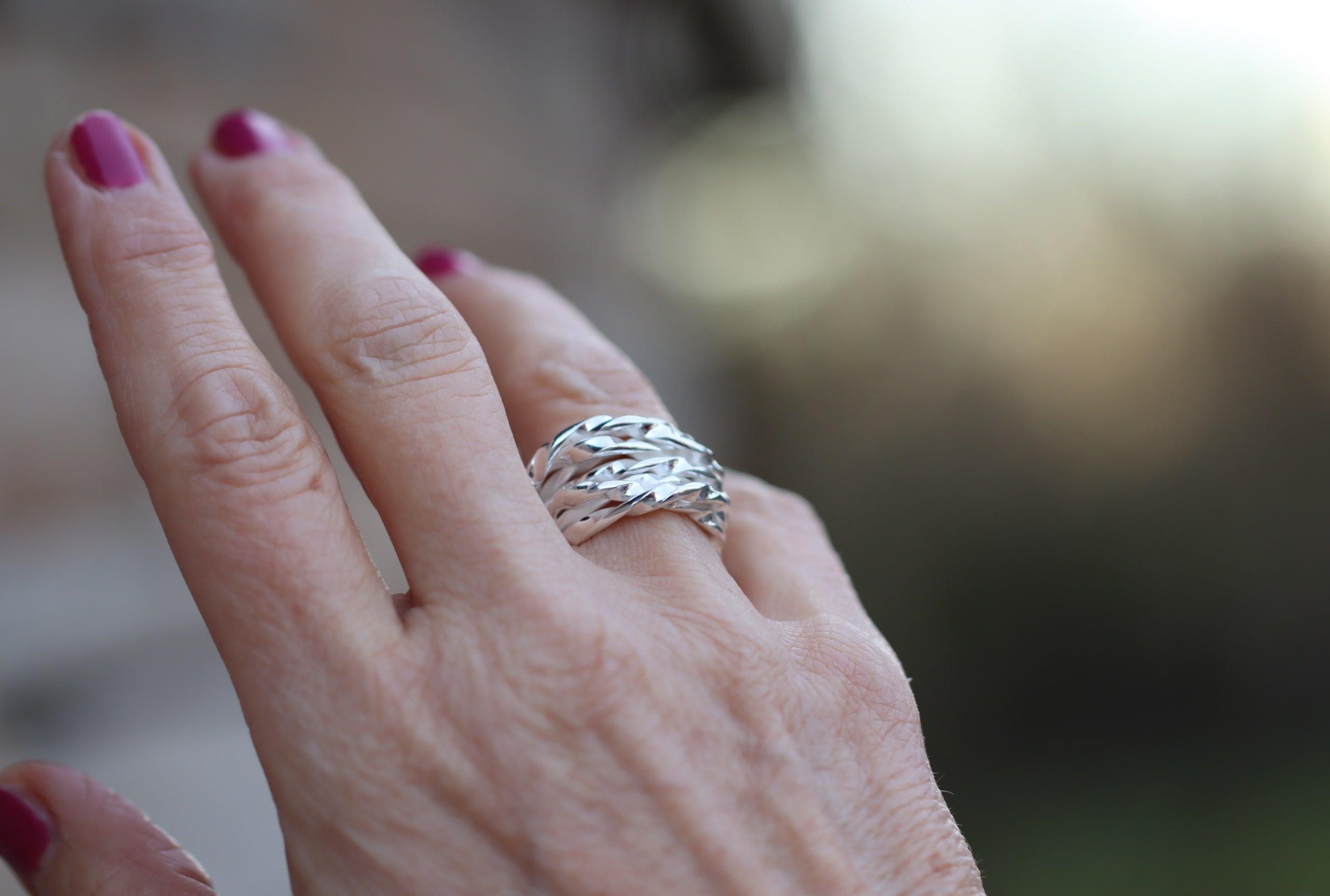Ein Wickelring aus Silber für Damen, gearbeitet aus einem schlanken leicht gekordelten Strang, der sich mehrfach um den Finger wickelt, getragen an einer Damenhand.