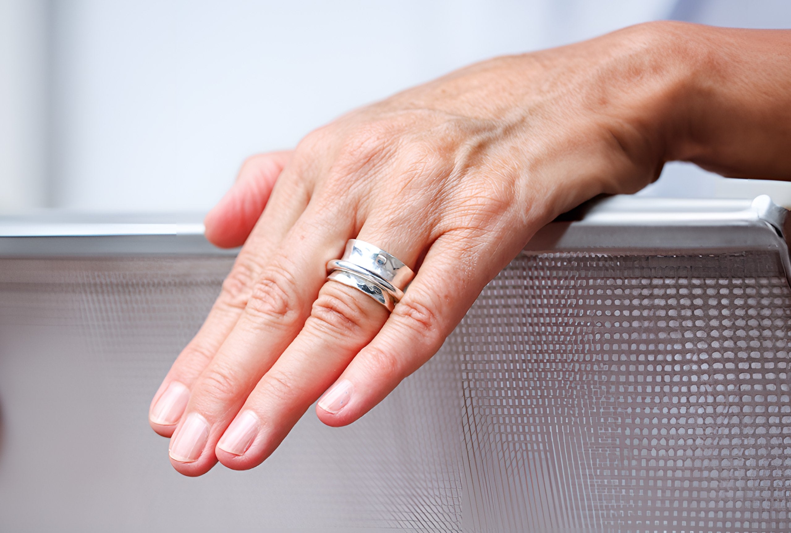 Ein moderner Schmiedering aus Silber getragen an einer Damenhand. Der Ring besteht aus einem massivem Bandring und einem kleinen Drehring, der unverlierbar darauf geschmiedet ist.