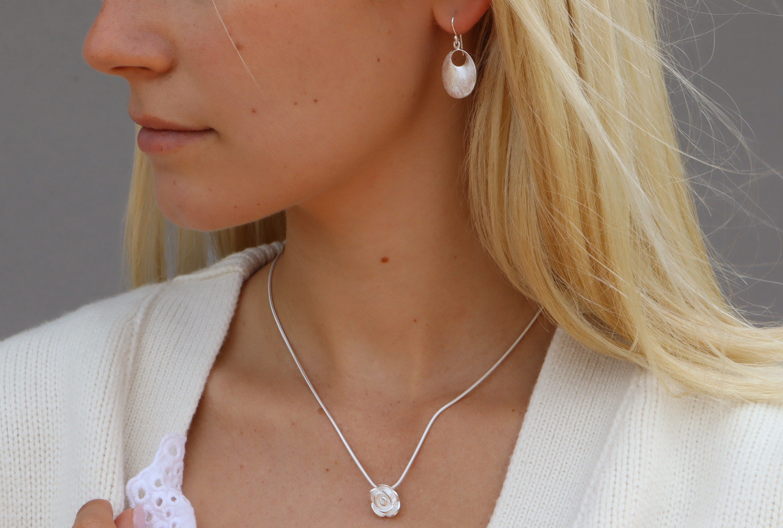 Klassische Ohrhänger aus Silber für Damen mit einer Öffnung und gebürsteter Oberfläche getragen am Ohr einer Dame.