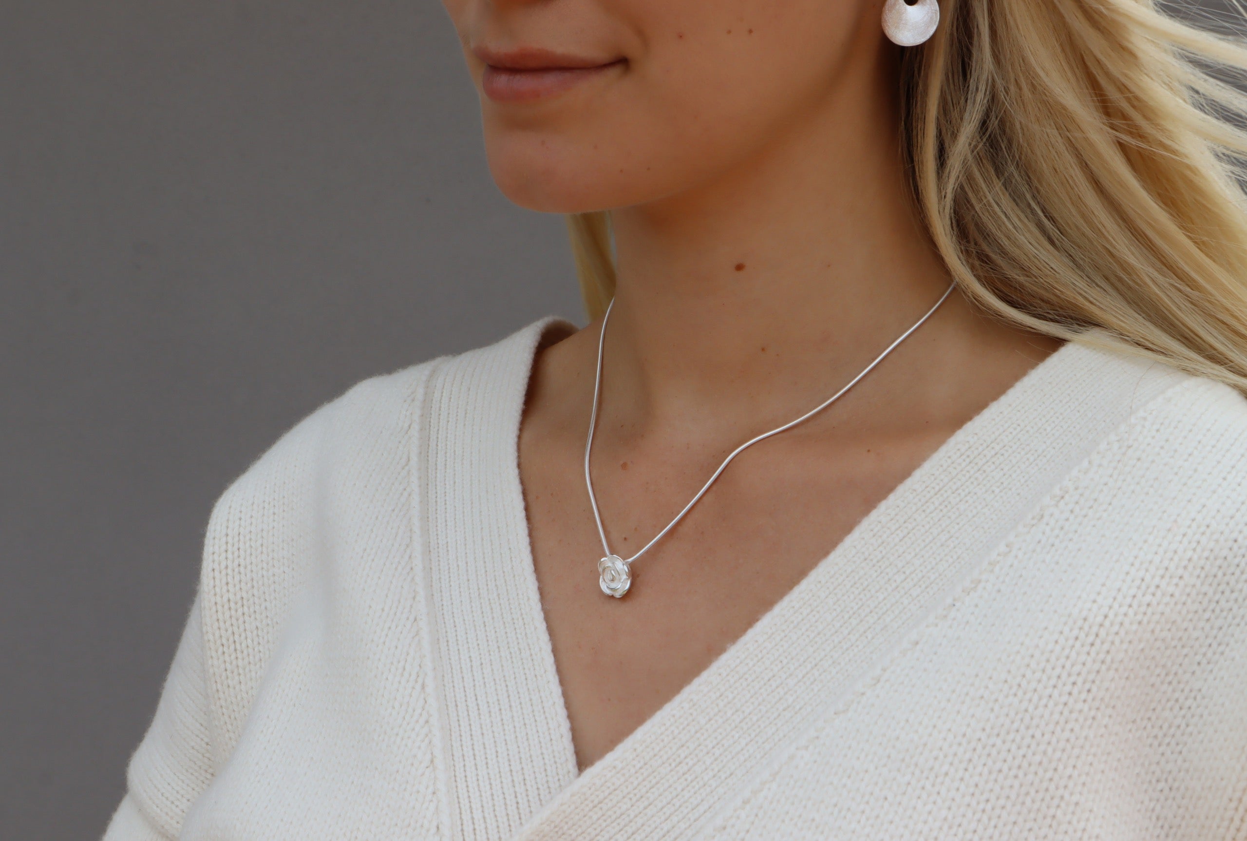 Eine Rose als Anhänger für Damen aus Silber mit sandgestrahlter Oberfläche und versenkten Ösen zum verdeckten Fädeln einer Kette.