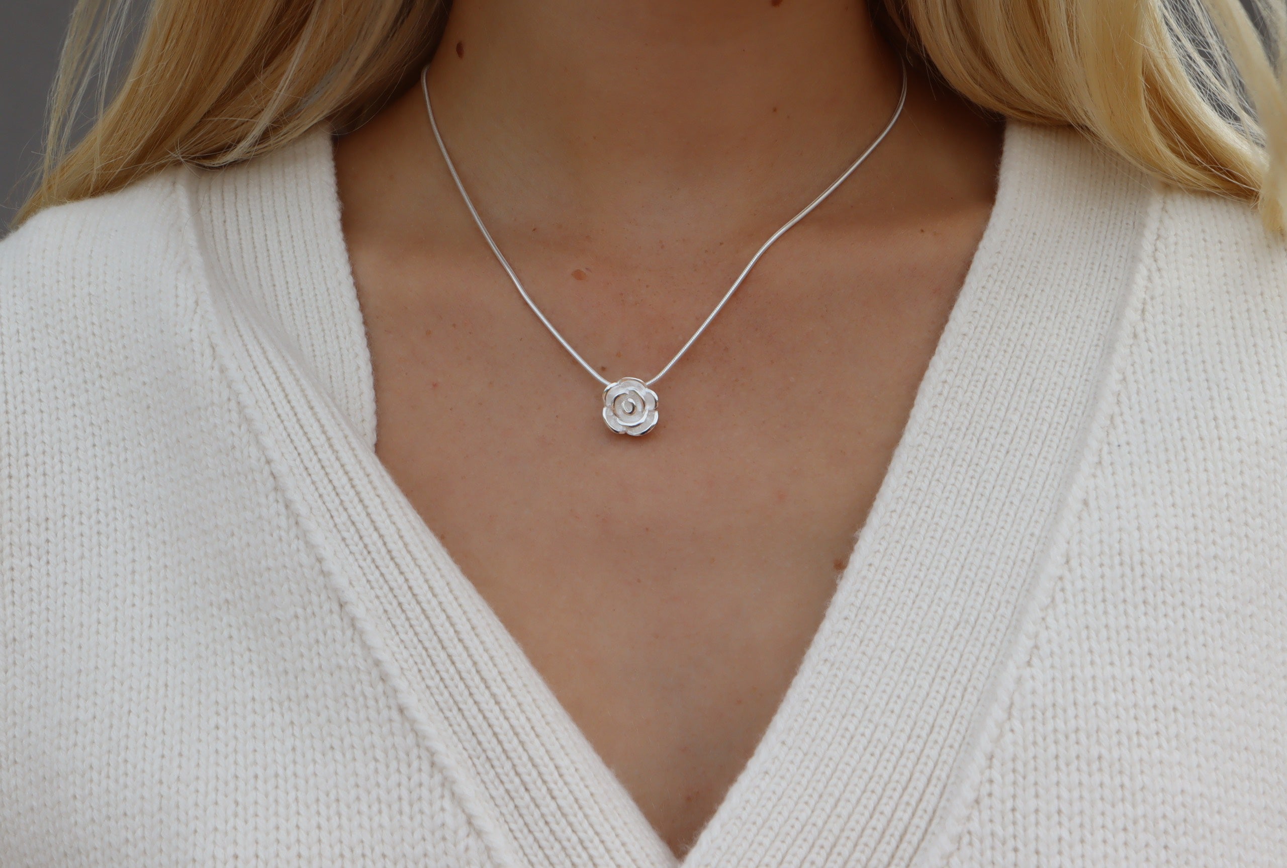 Eine Rose als Anhänger für Damen aus Silber mit sandgestrahlter Oberfläche und versenkten Ösen zum verdeckten Fädeln einer Kette.