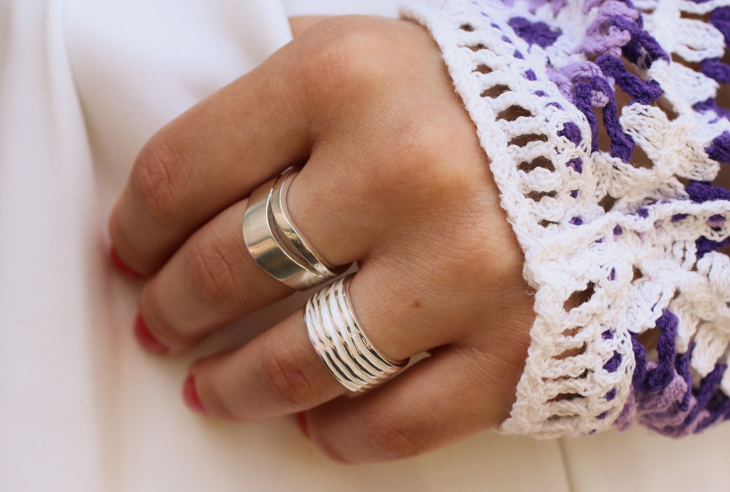 Ein Bandring aus Silber getragen an einer Damenhand, bestehend aus zwei kontastreich ineinander verschobenen Wellen mit fein mattierter Oberfläche.