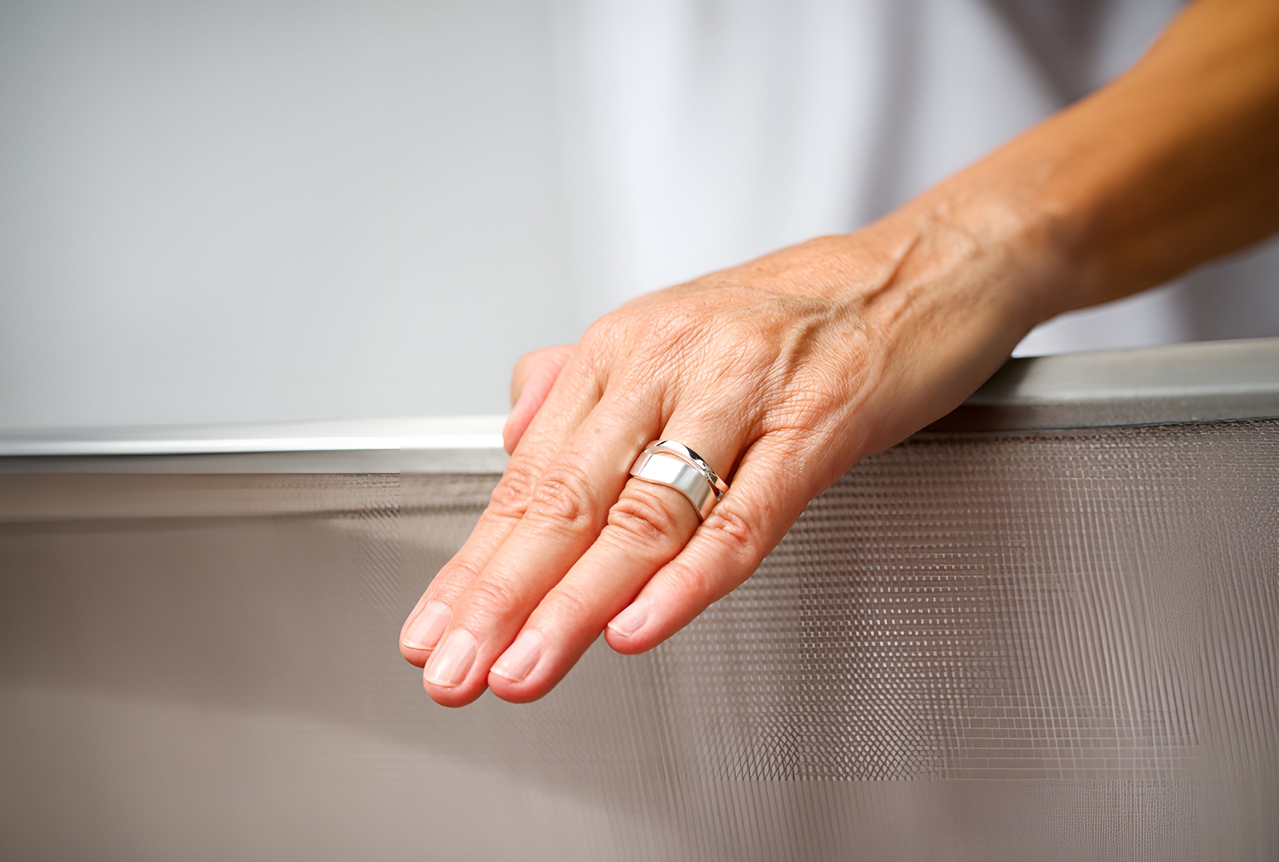 Ein Bandring aus Silber getragen an einer Damenhand, bestehend aus zwei kontastreich ineinander verschobenen Wellen mit fein mattierter Oberfläche.