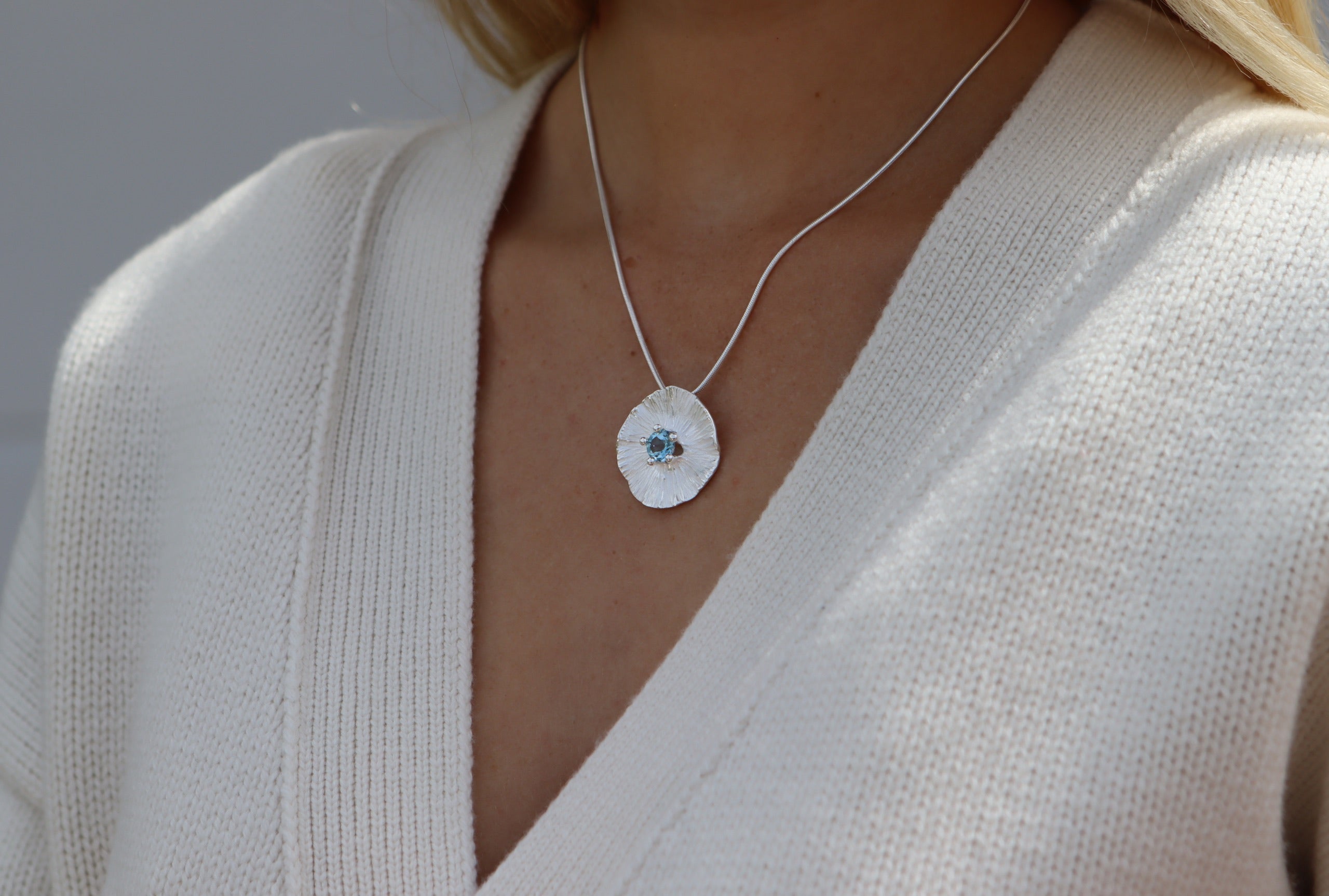 Runder Anhänger aus Silber für Damen mit fein modellierter Struktur mit einem mittig sitzenden Blautopas im Sternschliff.