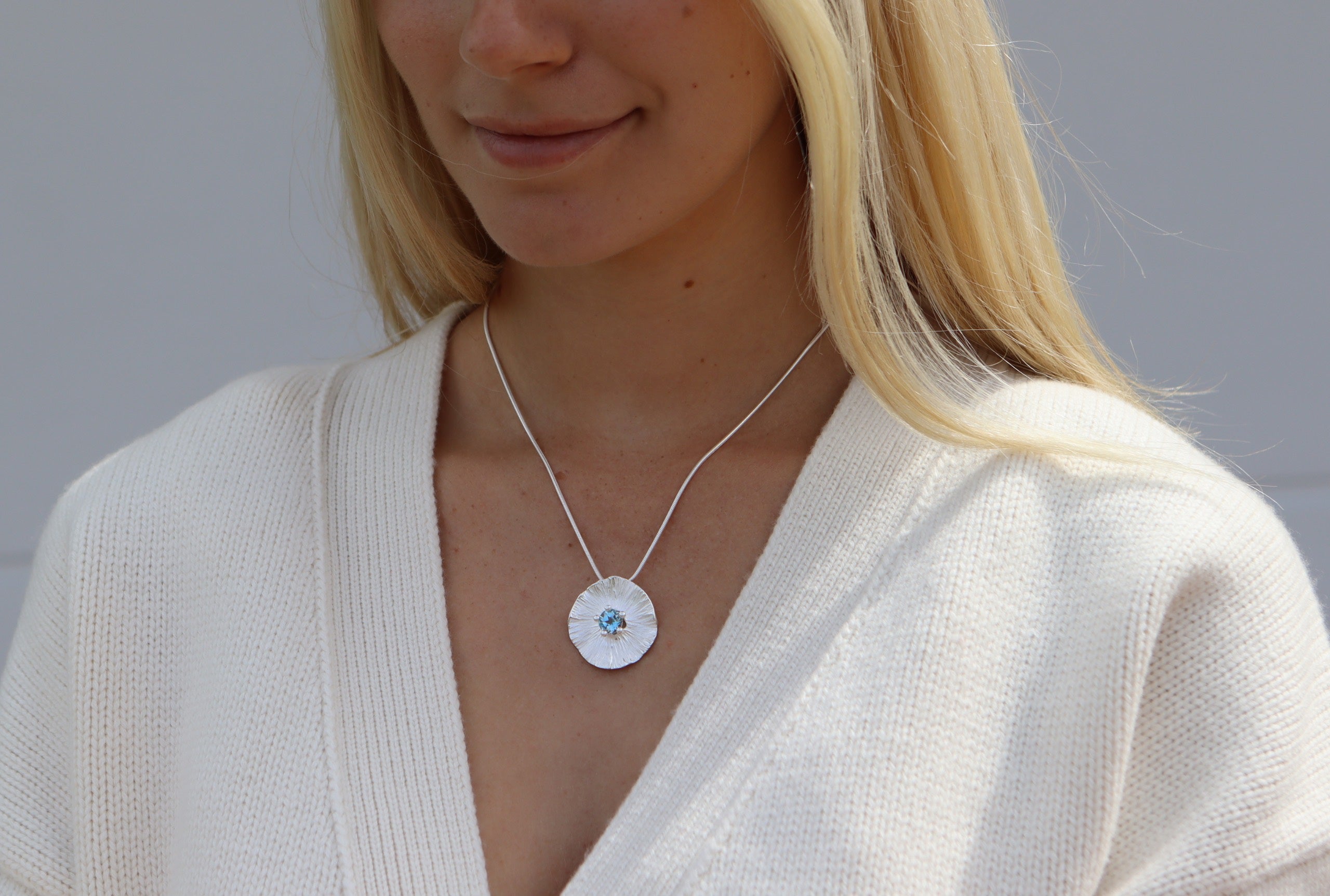 Runder Anhänger aus Silber für Damen mit fein modellierter Struktur mit einem mittig sitzenden Blautopas im Sternschliff.