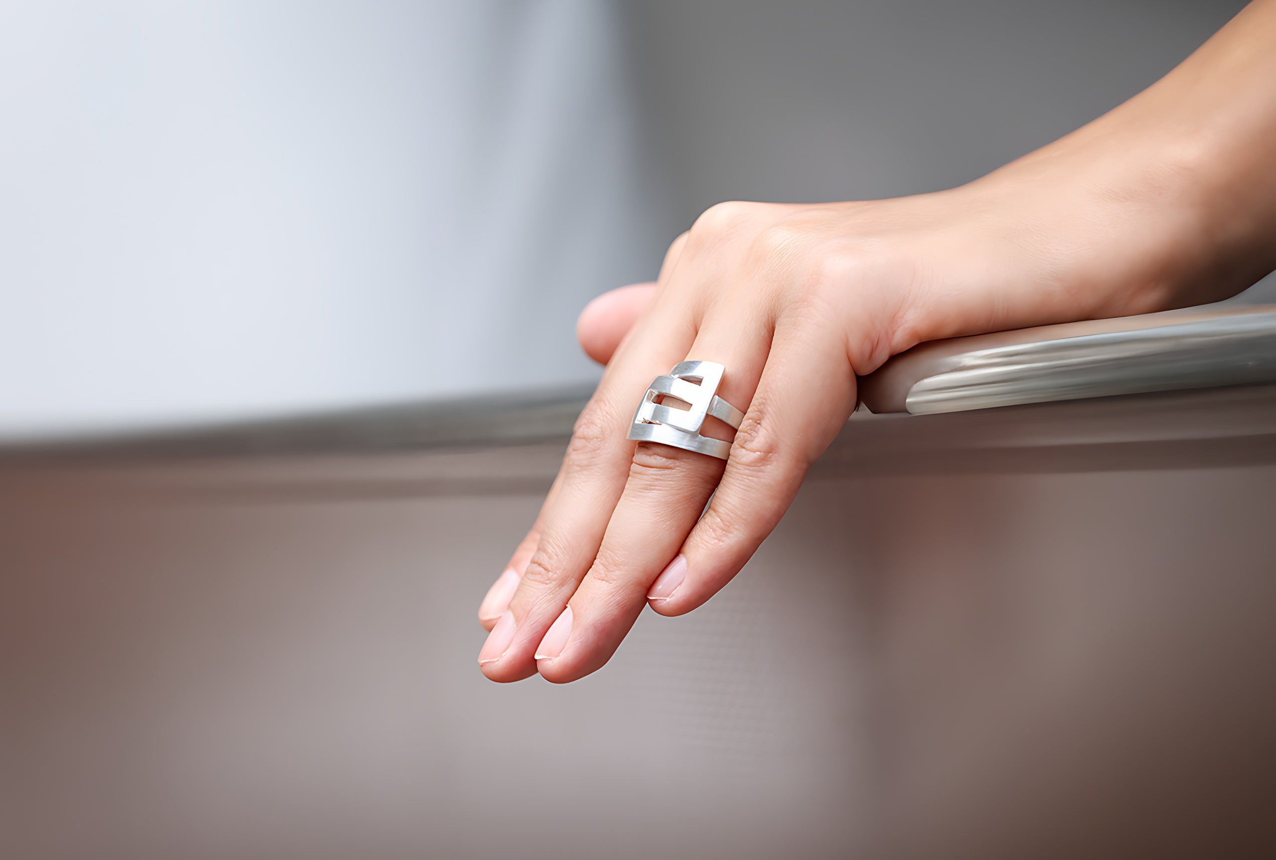 Ein Ring aus Silber für Damen, bestehend aus einer massiven Ringschiene und zwei ineinander greifenden Vierecken, getragen an einer Damenhand.