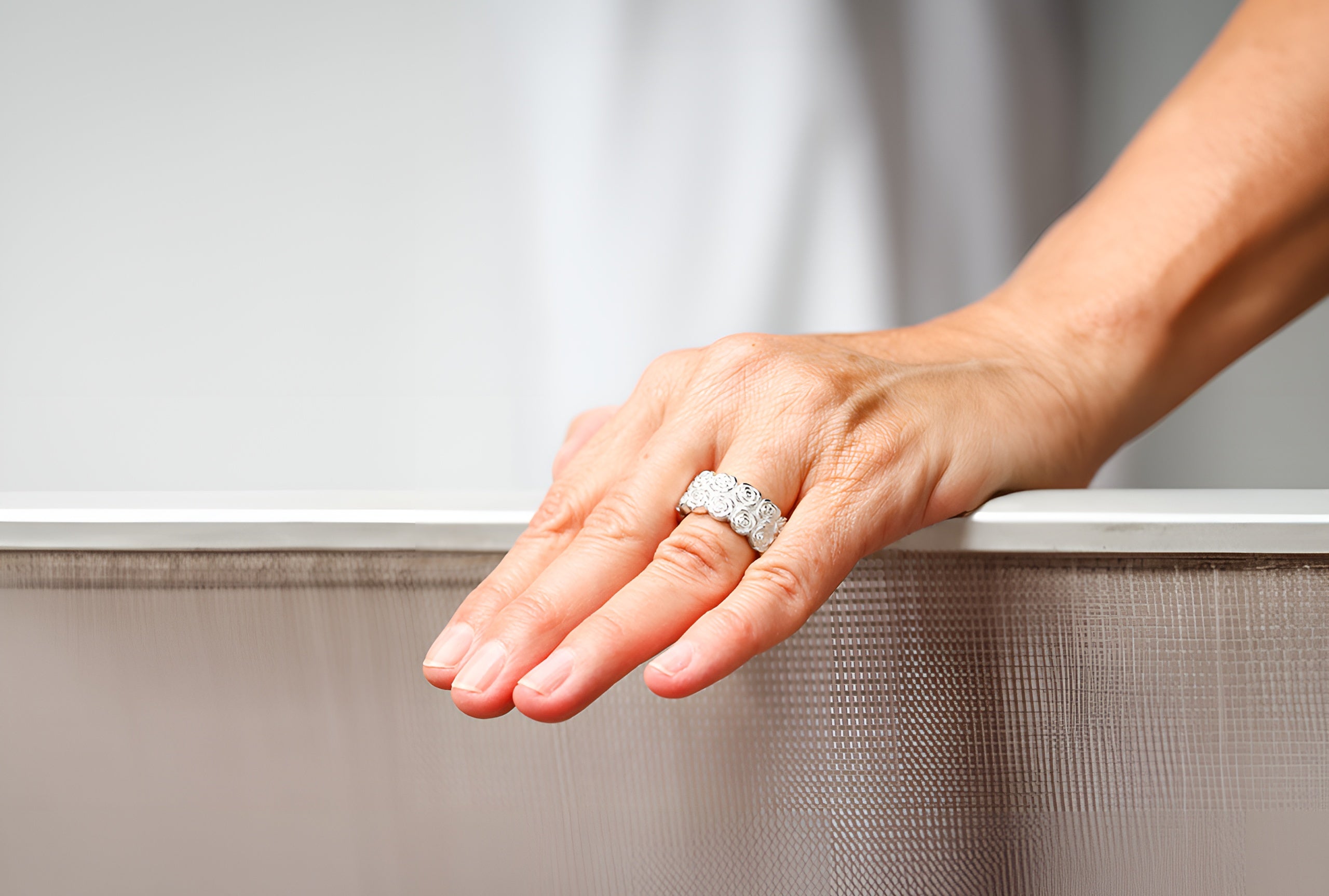 Ein massiver Rosenring aus Silber, getragen an einer Damenhand. Er ist als Bandring gearbeitet und zeigt als Motiv zwei Reihen filigraner Rosenblüten.