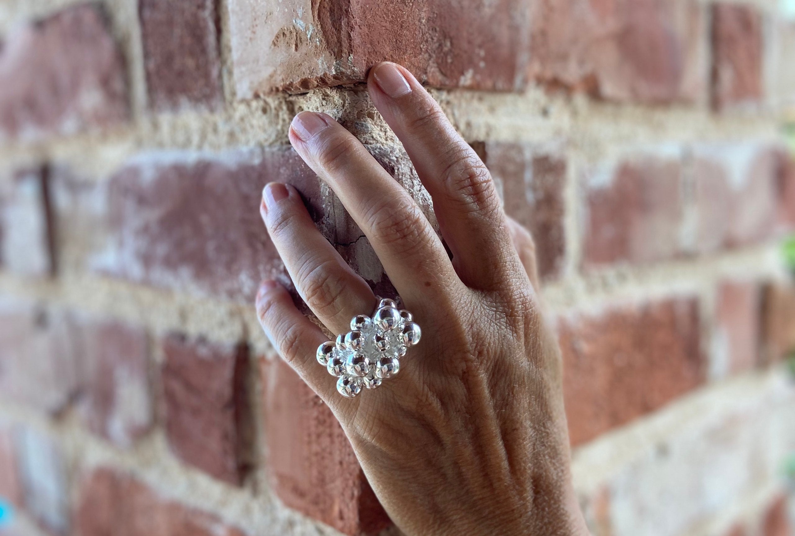 Ein opulenter Designring mit großen dekorativen Kugeln aus Silber, getragen an einer Damenhand.