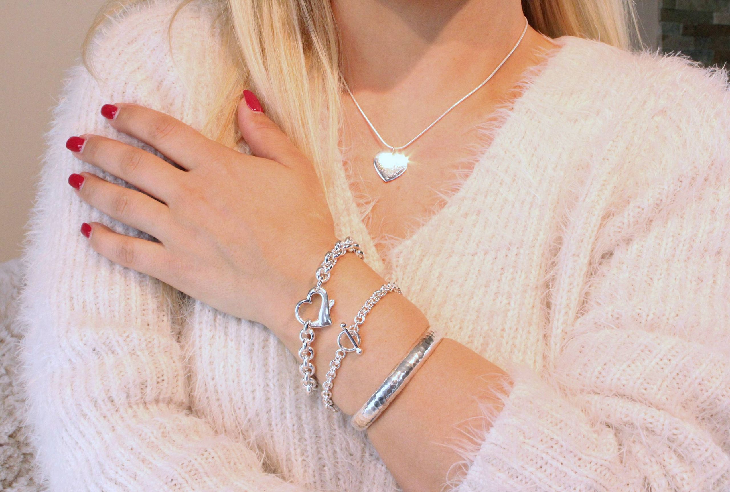 Ein massives Herzarmband aus Silber für Damen mit einem dekorativen Herz als Verschluss, getragen am Handgelenk einer Dame.