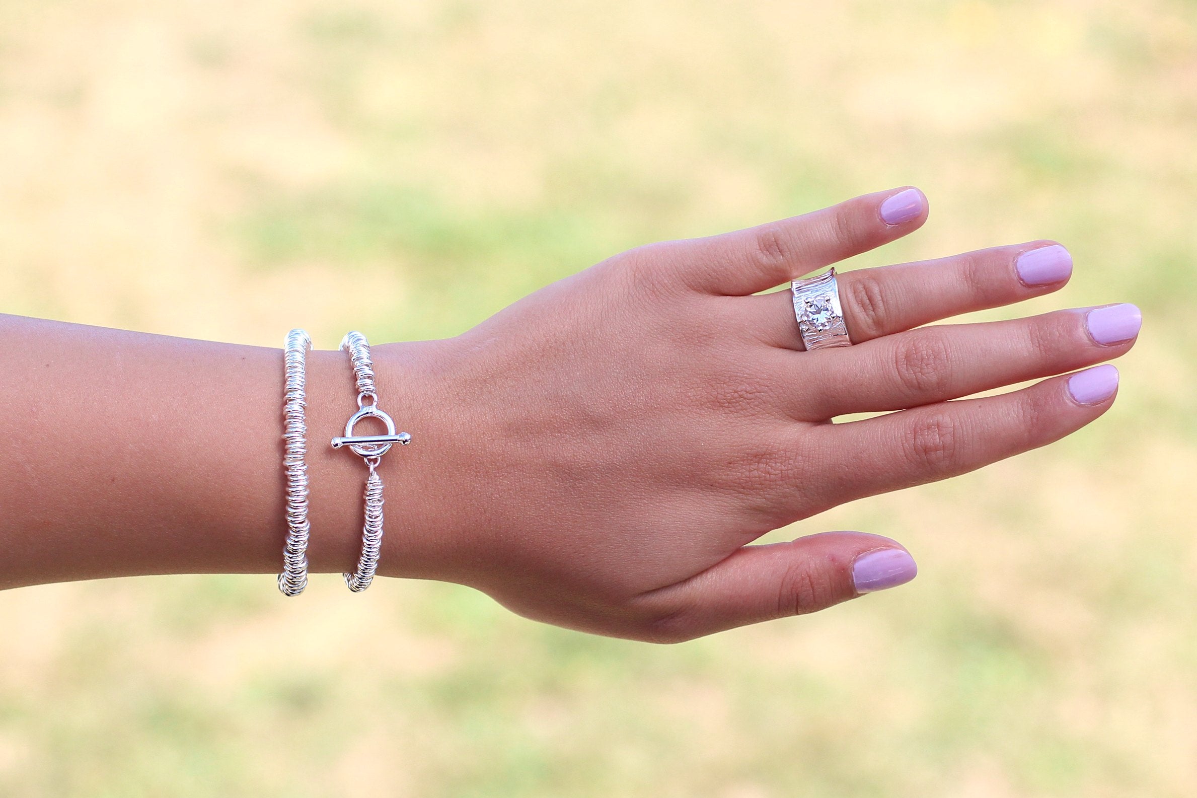 Ein Silberarmband aus vielen kleinen Silberringen mit einem dekorativen Verschluss, getragen am Handgelenk einer Dame.
