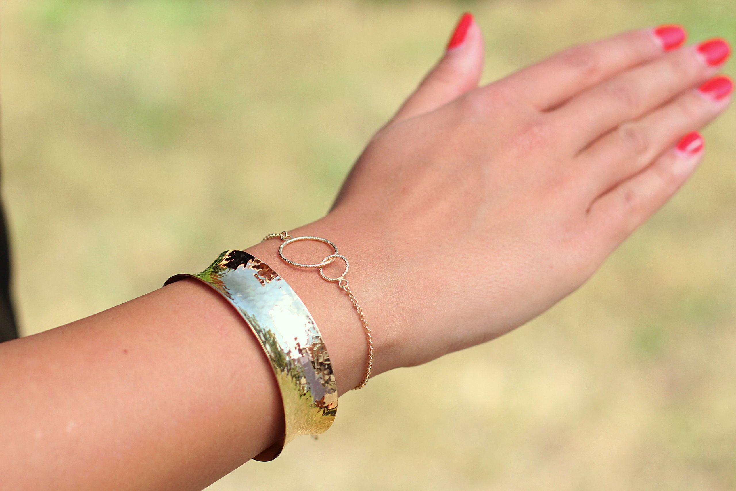 Ein Armband aus gold-plattiertem Silber aus einer Ankerkette mit zwei ineinander greifenden Kreisen, getragen am Handgelenk einer Dame.