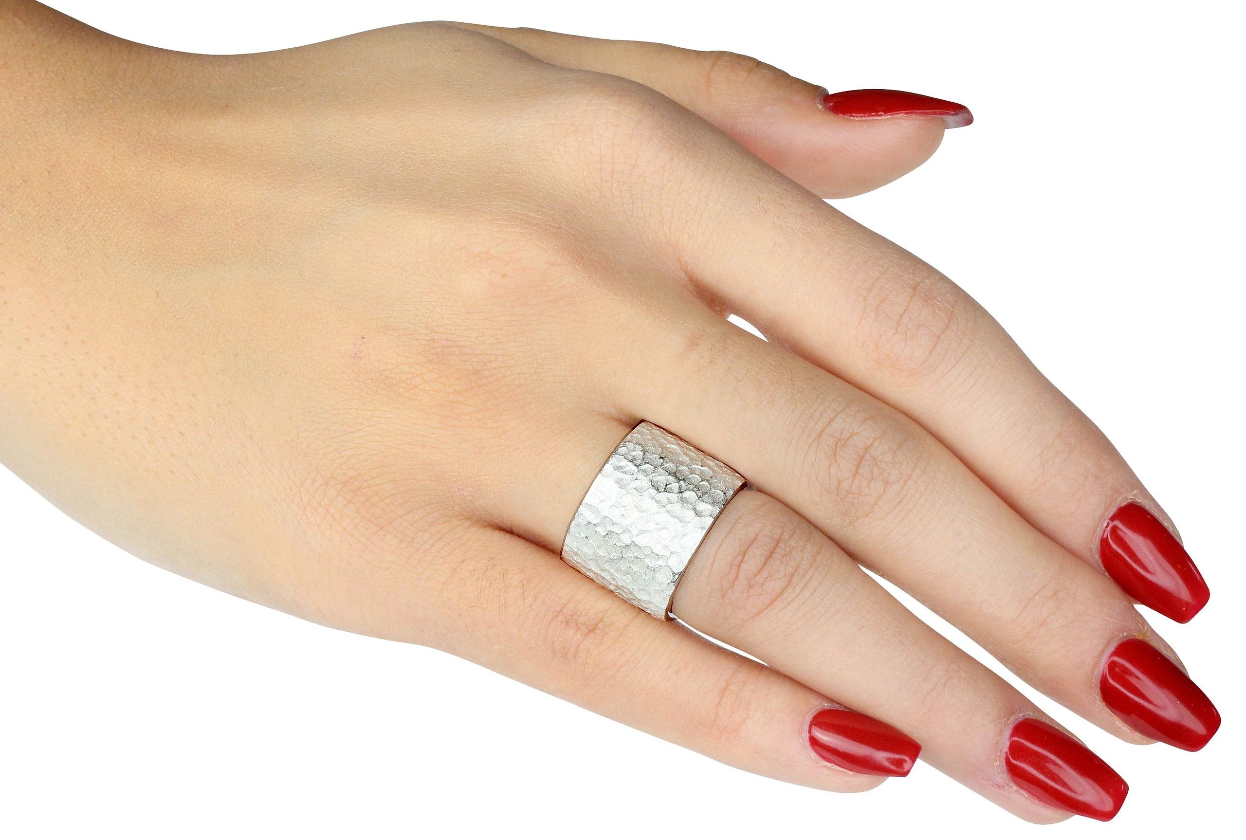 Ein breiter Damenring aus Silber mit einer gehämmerten Struktur-Oberfläche, getragen an einer Damenhand.