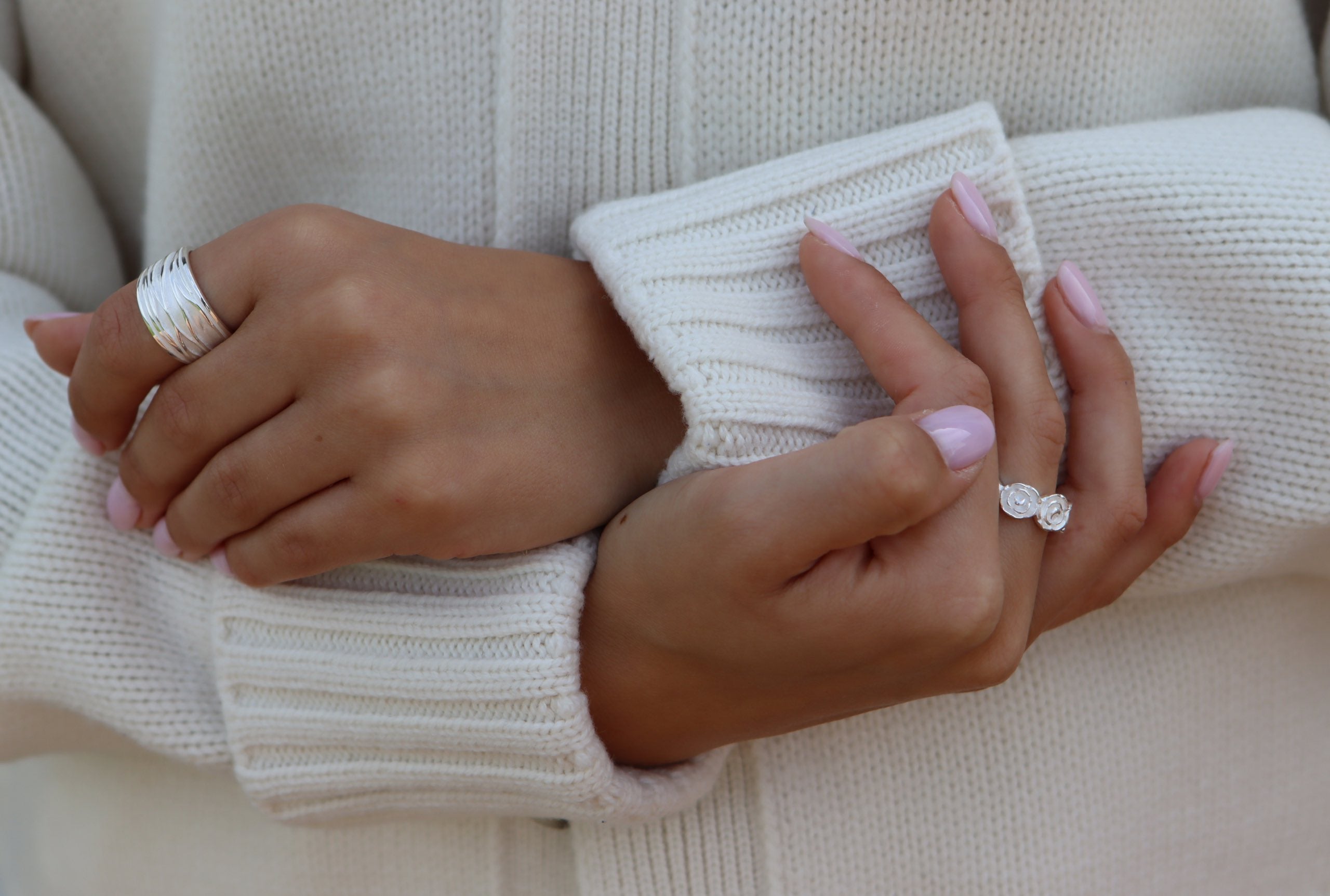 Ein Silberring für Damen mit einer gefalteten Wellenstruktur als Oberfläche getragen an einer Damenhand, wobei sich die Ringschiene nach unten hin verjüngt.