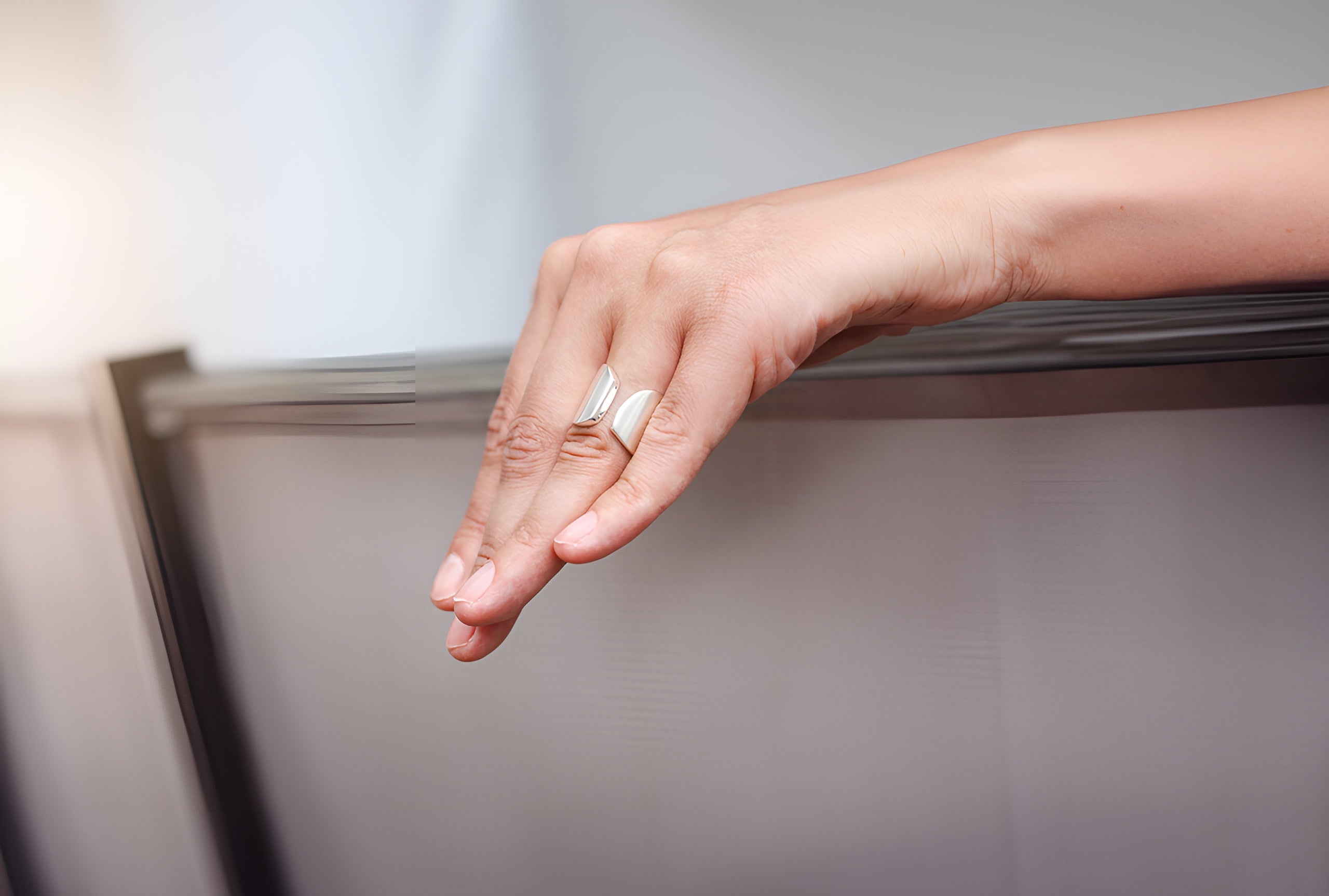 Ein offen gearbeiteter Bandring aus Silber für Damen mit einer mattierten Oberfläche getragen an einer Damenhand.