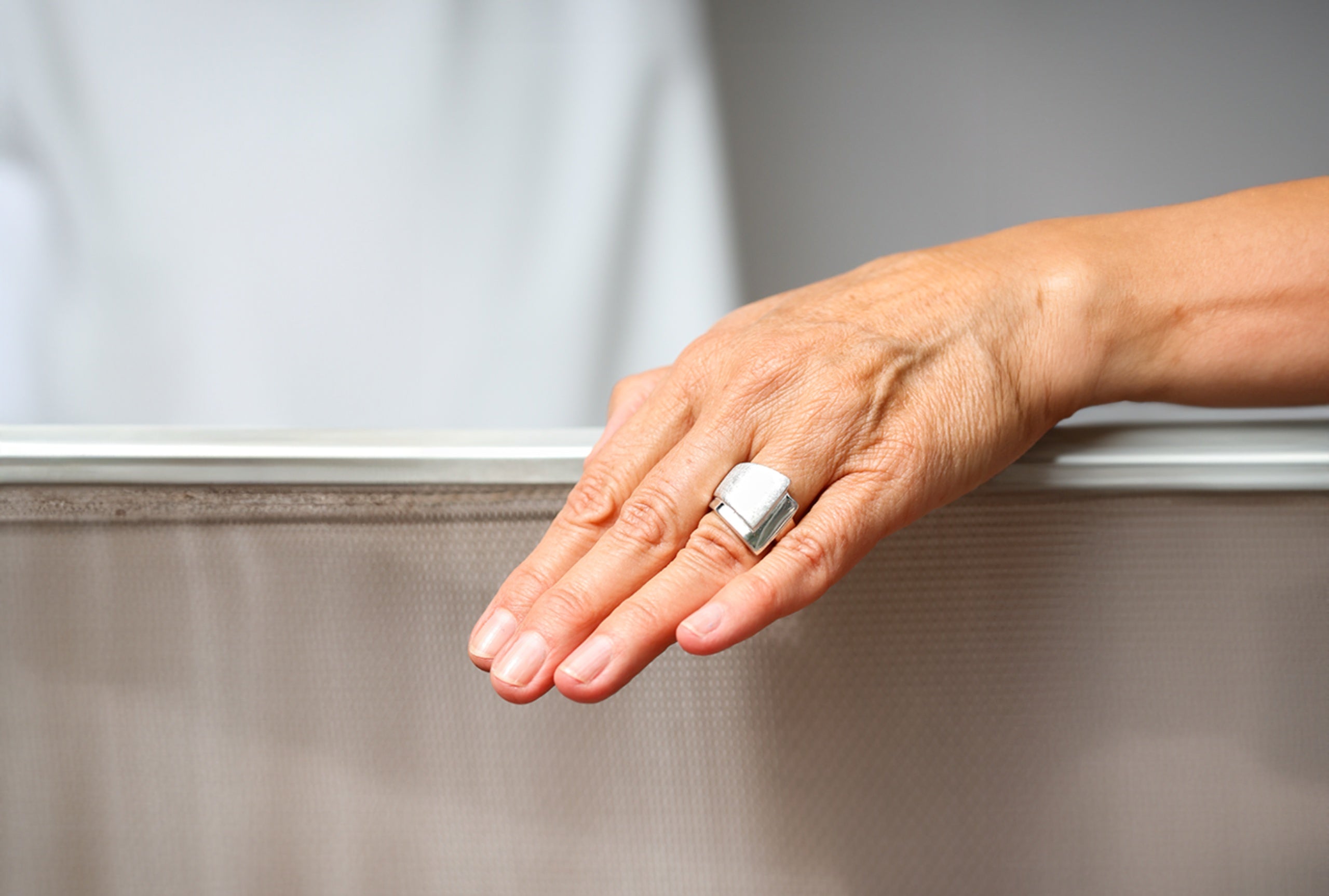 Ein Bandring aus Silber für Damen, bei dem ein oberer gebürsteter Ring mit einem unteren glänzenden Ring zu einem Schmuckstück verschmilzt, getragen an einer Damenhand.