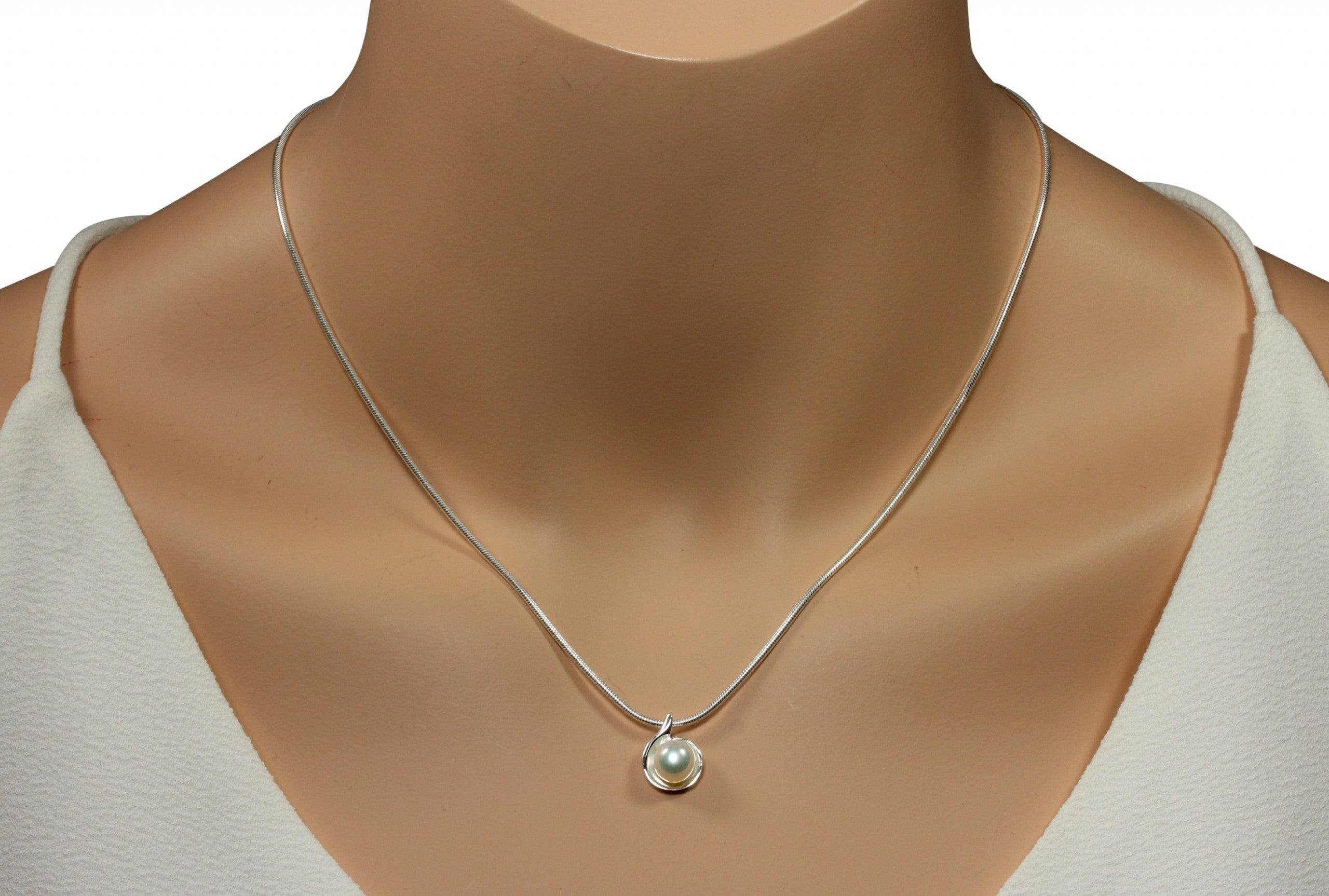 Ein glänzender Perlenanhänger aus Silber für Damen getragen mit einer klassischen Schlangenkette an einer Schaufensterpuppe.
