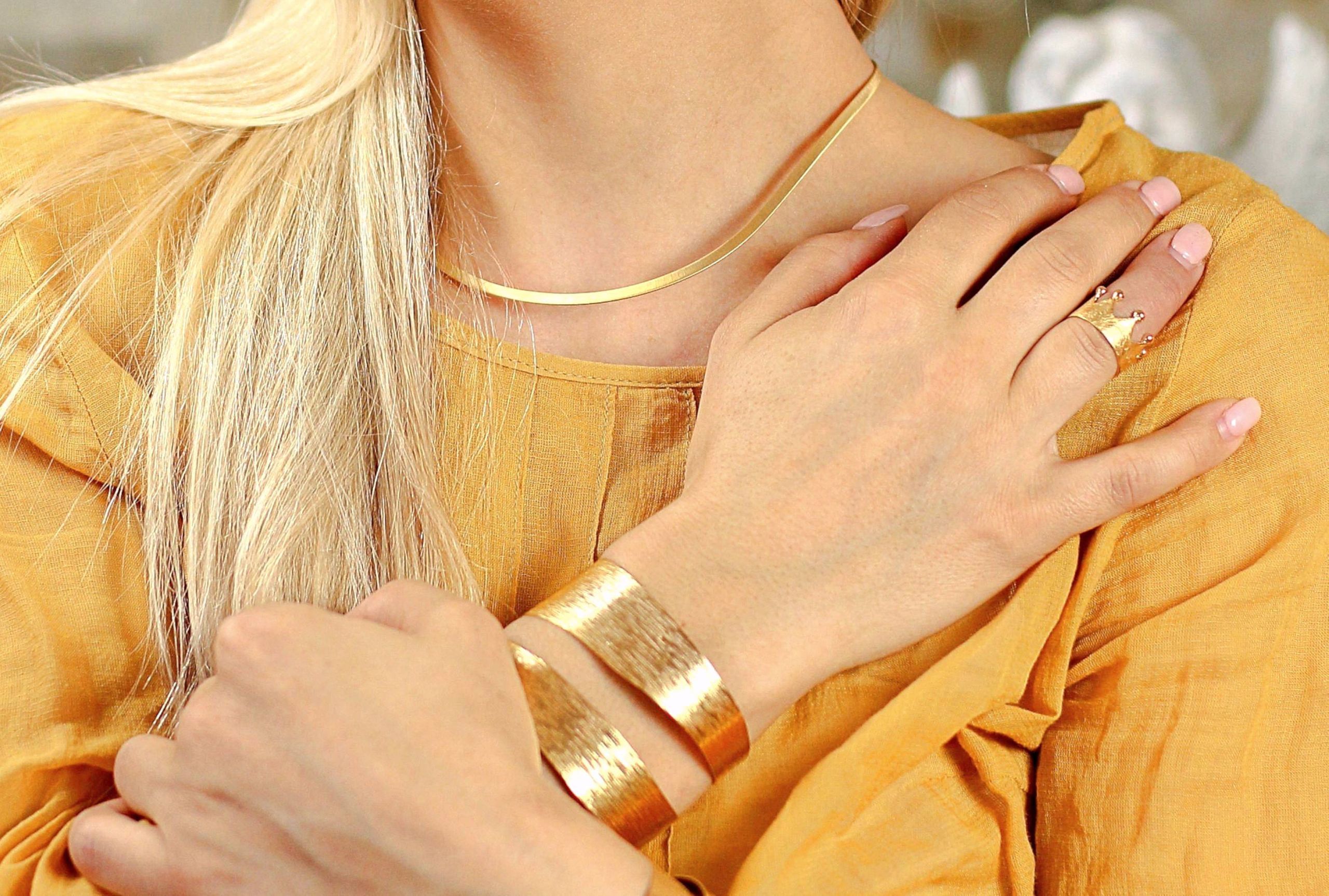 Ein Armreif aus Silber mit vergoldeter Oberfläche, den eine diagonale Aussparung und eine gewellte Oberflächenstruktur zum Blickfang machen, getragen an einer Damenhand.