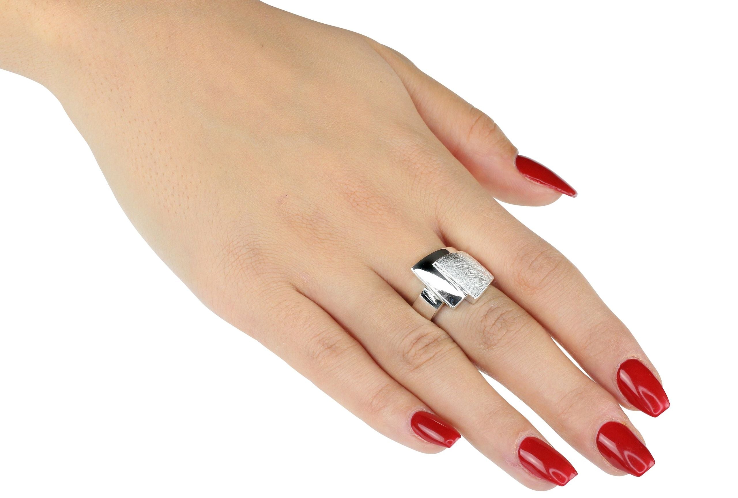 Ein Bandring aus Silber für Damen, bei dem ein oberer gebürsteter Ring mit einem unteren glänzenden Ring zu einem Schmuckstück verschmilzt, getragen an einer Damenhand.