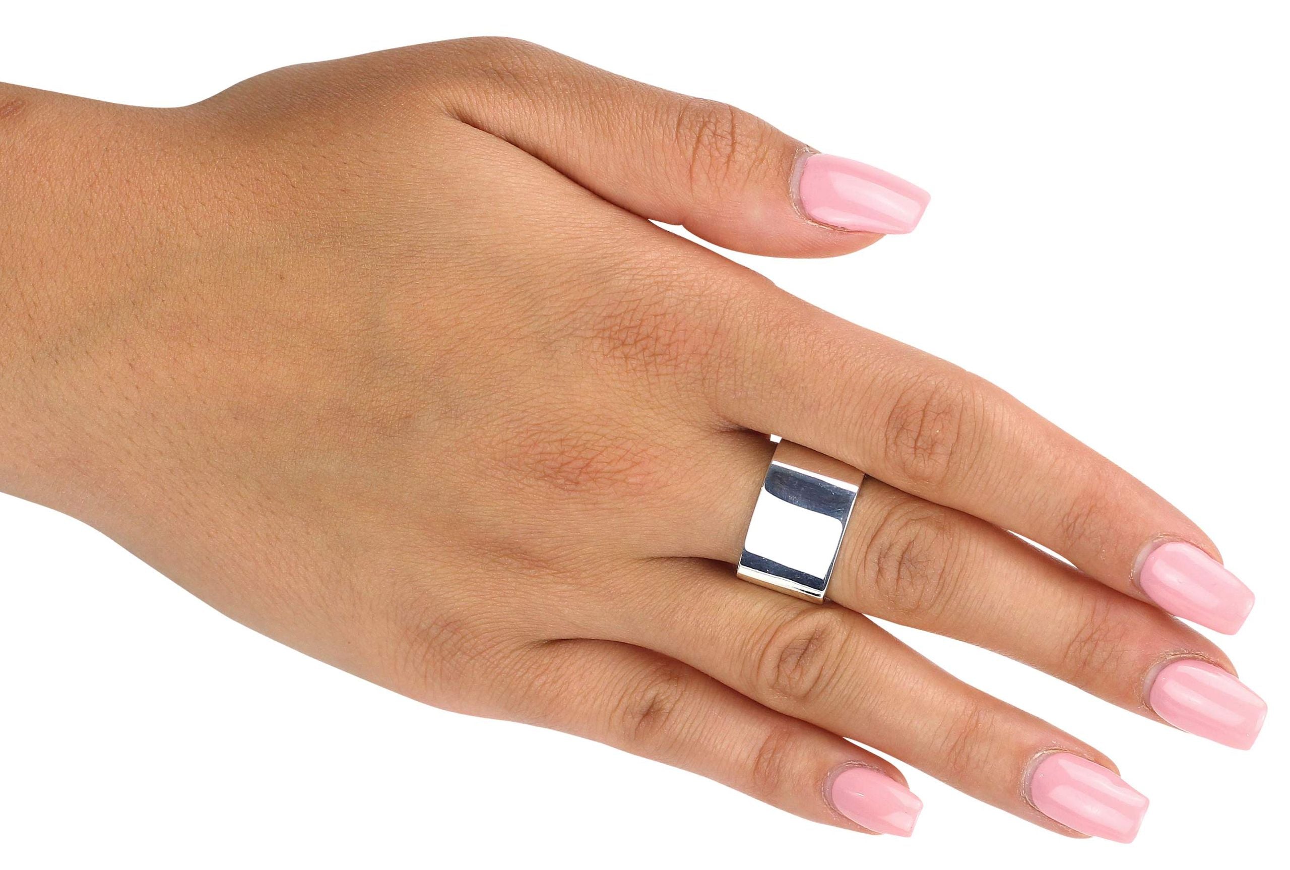 Ein geschmiedeter viereckiger Ring aus Silber mit einer glänzend polierten Oberfläche, getragen an einer Damenhand.