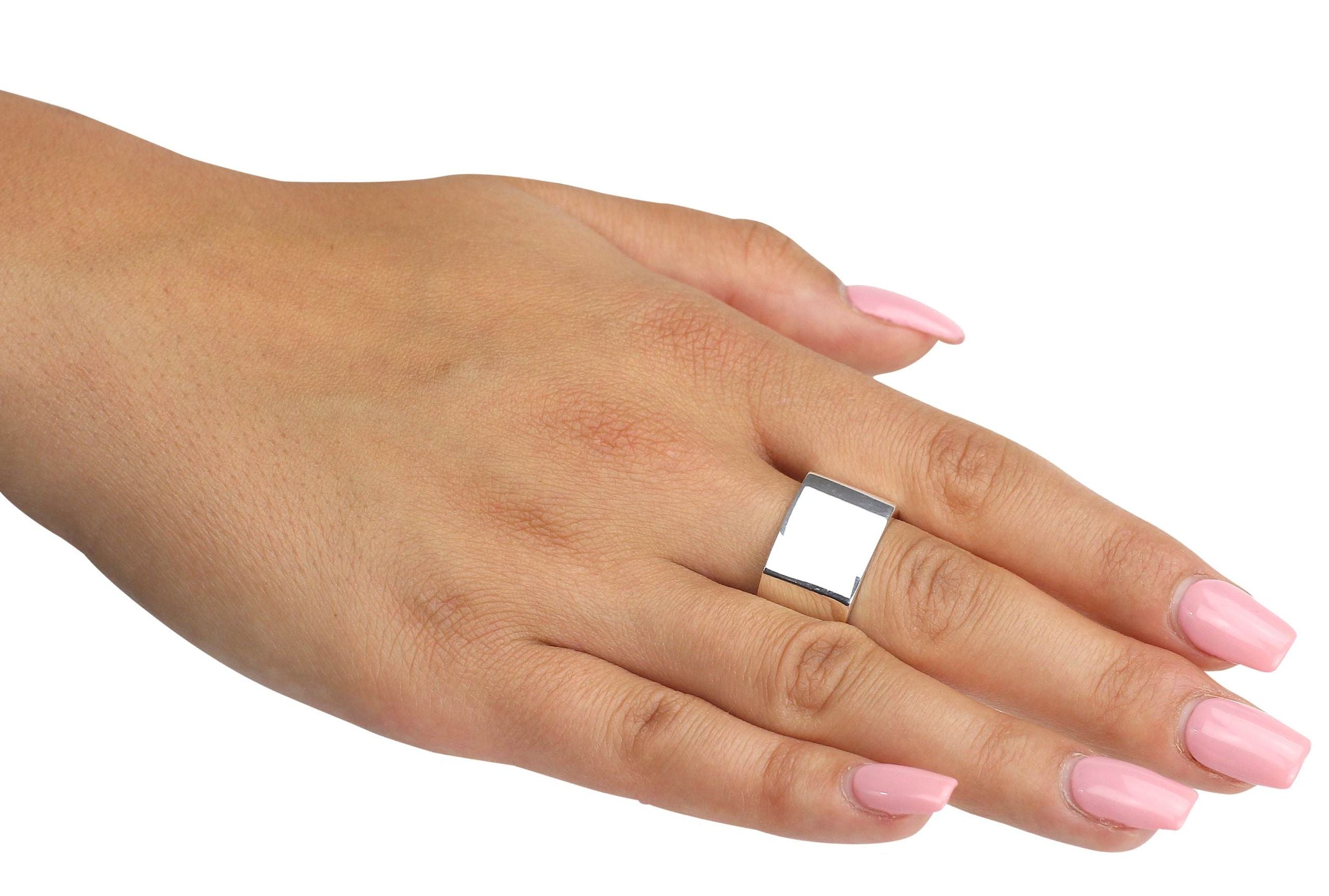 Ein geschmiedeter viereckiger Ring aus Silber mit einer glänzend polierten Oberfläche, getragen an einer Damenhand.