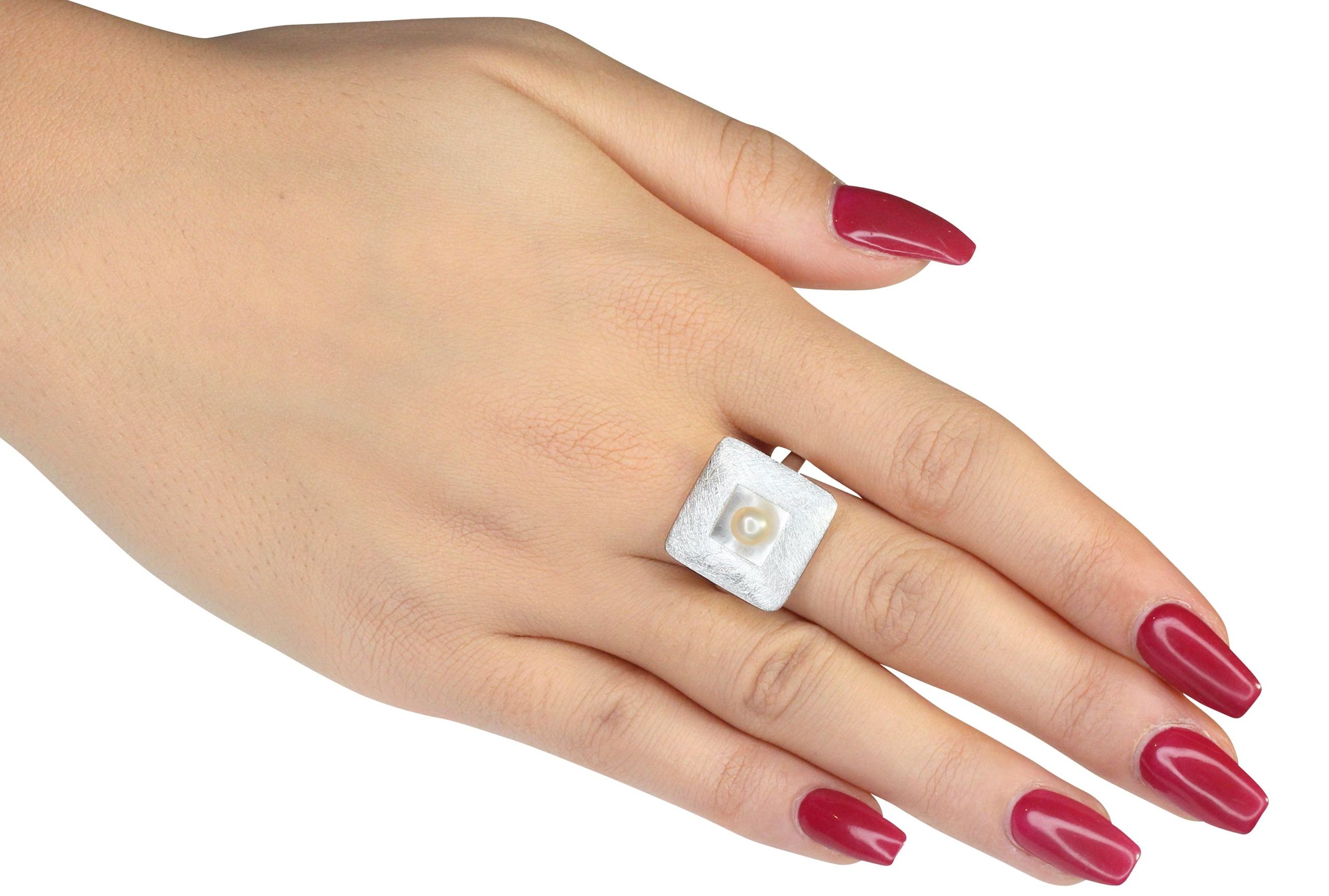 Ring aus Silber mit einer Perle getragen an einer Damenhand. Die Perle sitzt mittig in einem quadratischen Zierelement und die Ringschiene ist klassisch gearbeitet.