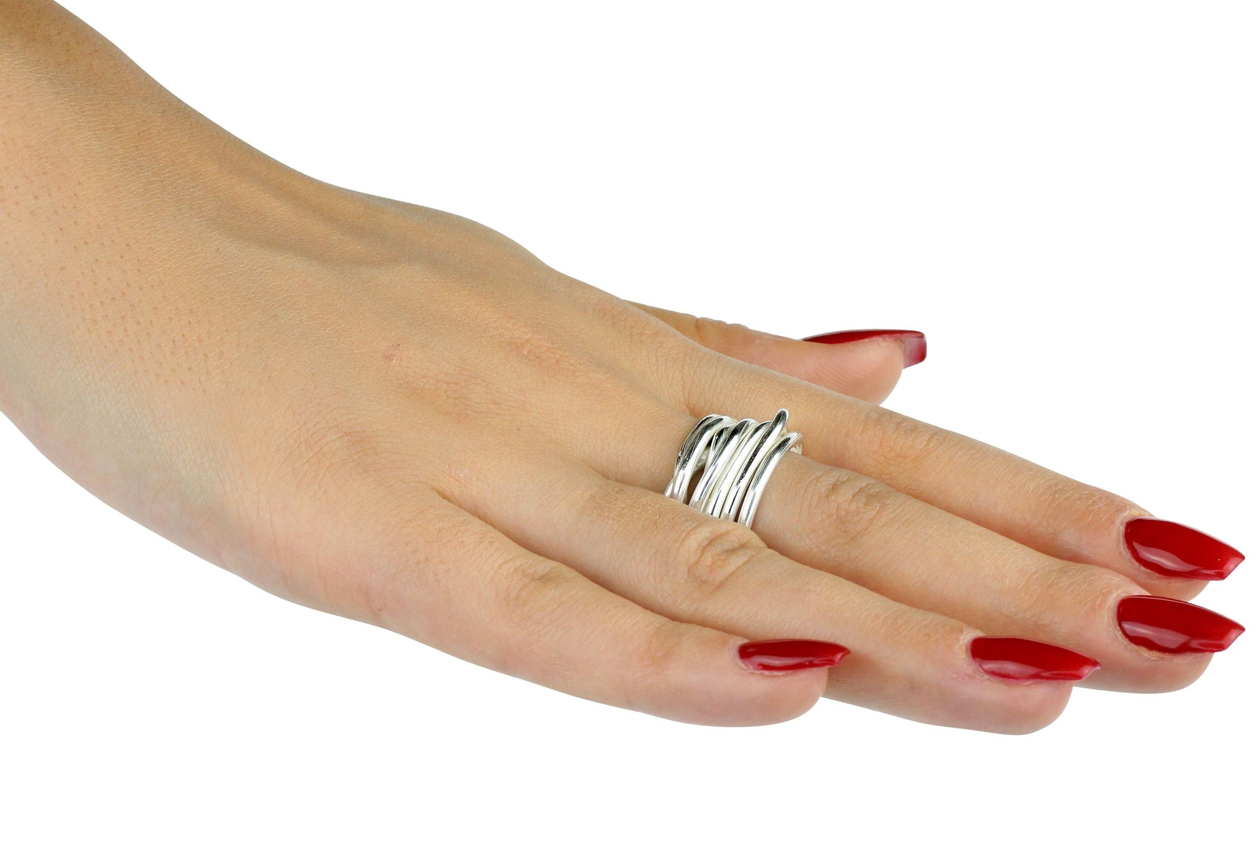 Ein Wickelring aus Silber für Damen bestehend aus sieben einzelnen Silbersträngen, die fest miteinander verbunden sind und dabei zusammen einen Ring formen, getragen an einer Damenhand..