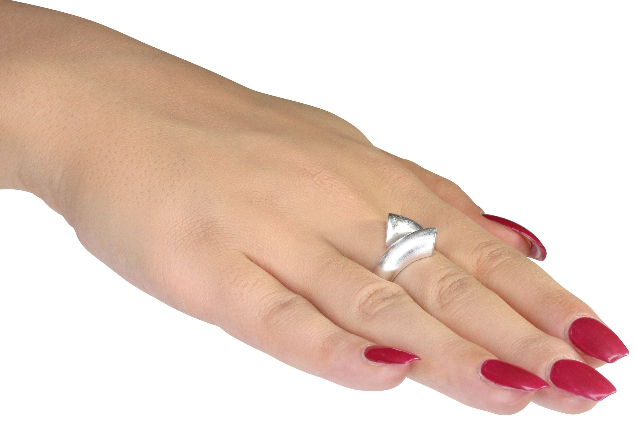 Geschwungener Ring aus Silber getragen an einer Damenhand, dessen Enden nicht verbunden sind und einander offen gegenüberstehen.