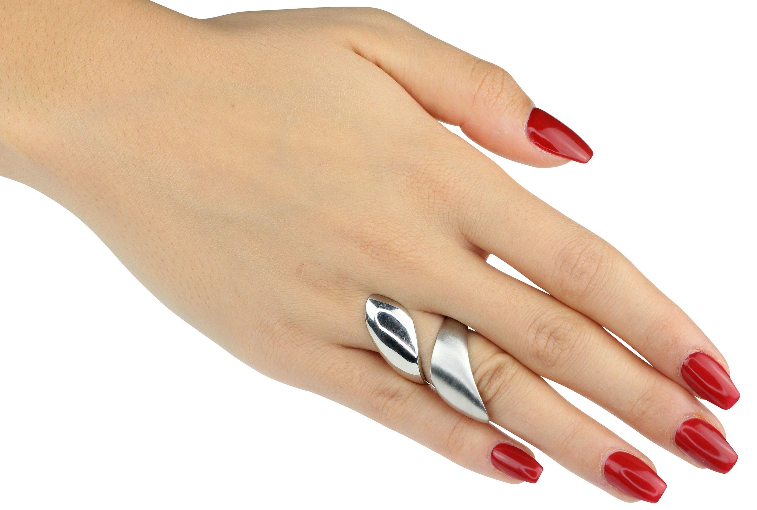 Ein offener  Ring aus Silber getragen an einer Damenhand. Der Damenring besitzt eine teils matt, teils glänzend gearbeitete Oberfläche, der mit seiner Form eine Umarmung um den Finger andeutet.